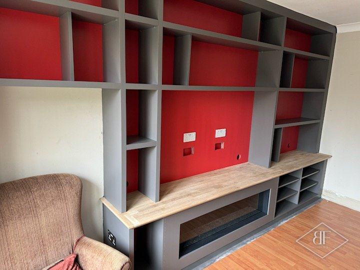 Finished media wall with red backed shelving, oak top and recessed electric fire