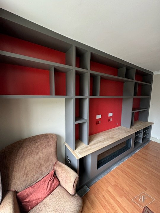 Side view of completed grey shelving unit with red panels beside an armchair