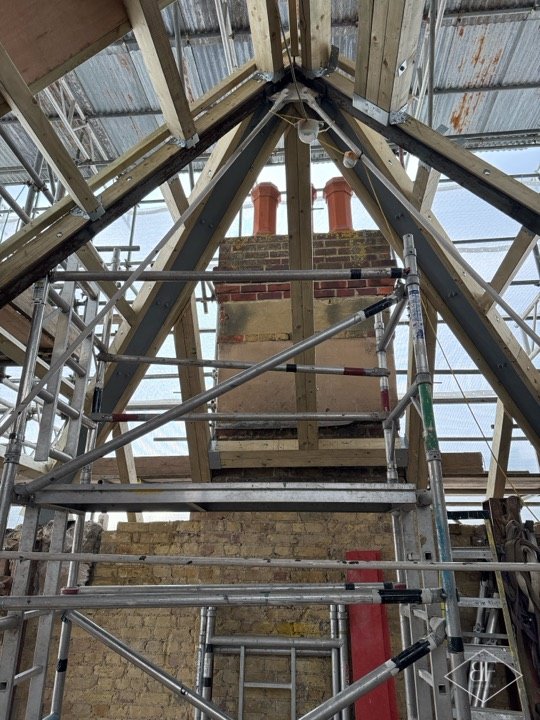 Roof structure rising around a brick chimney stack inside scaffolding