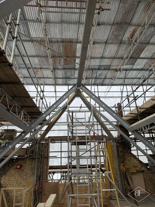 Steel and timber roof trusses forming a peak above a scaffolded space