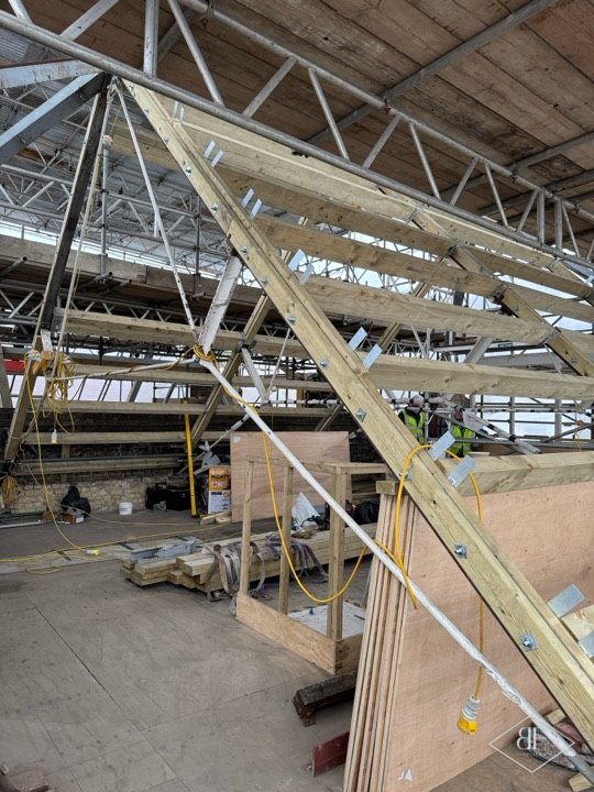 New timber roof beams with bolted joints sloping across a large roof space