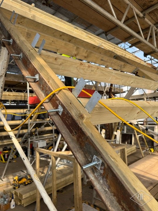 Timber rafters fixed with metal brackets to a steel beam during roof installation