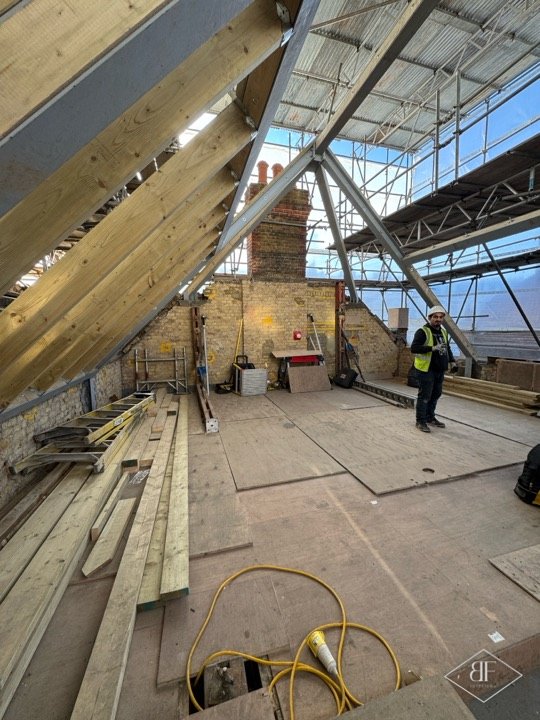 Wide view of new timber rafters rising above the plywood-decked floor