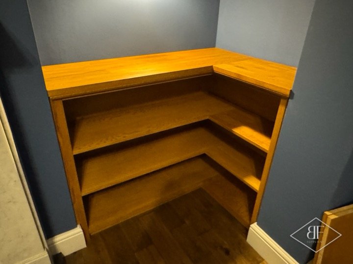 Tiered oak shelving fitted into a corner alcove with an oak top