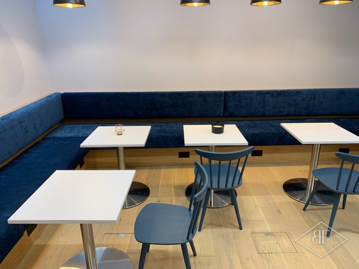 Built-in blue velvet banquette running along the wall with café tables in front