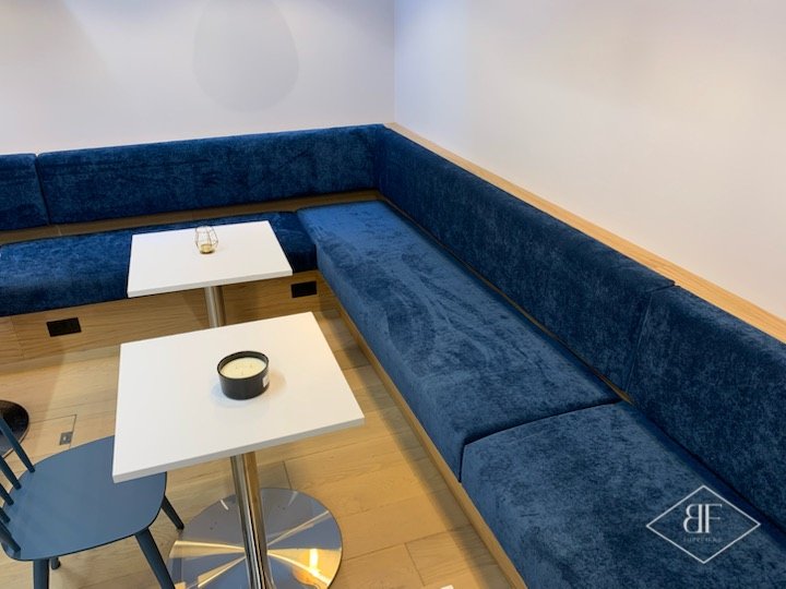 Corner of the blue upholstered bench seating with a timber trim along the wall