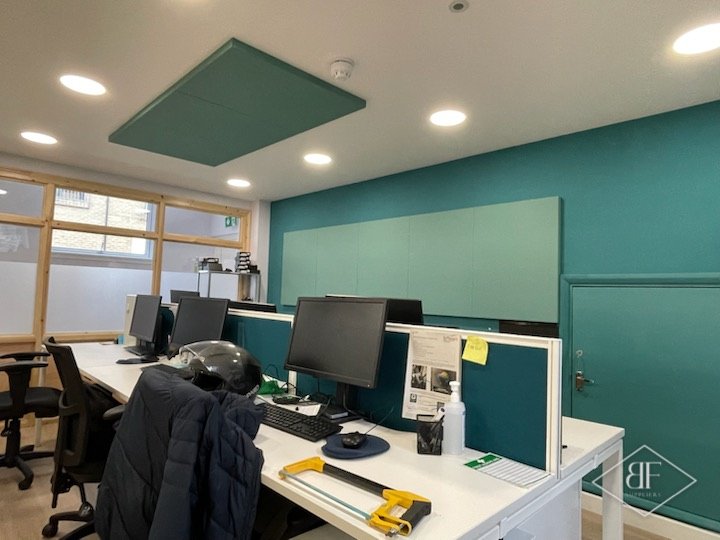 Desk area with teal wall, acoustic ceiling panel and monitors on white desks