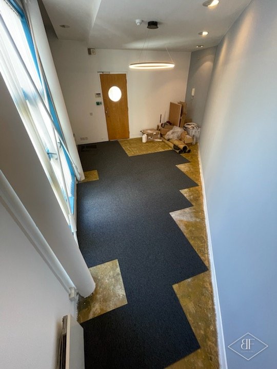 Dark carpet tiles spreading across an office floor towards a timber door