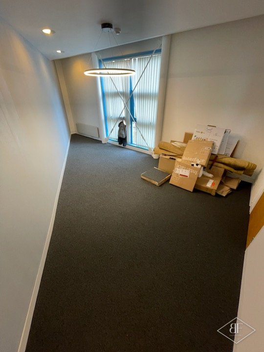 Small finished office with dark carpet tiles and a bright window