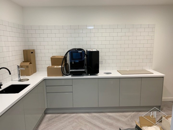 White metro-tiled wall above grey units, white worktop and coffee machine