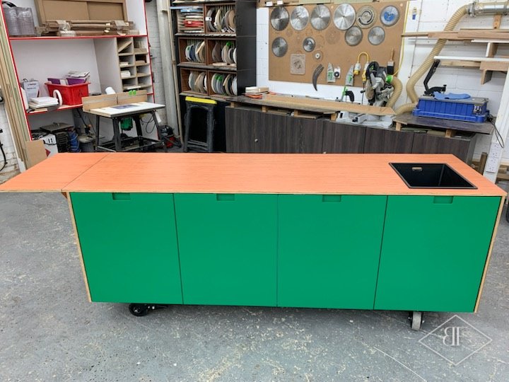 Mobile green kitchen island with orange top and inset sink in a workshop