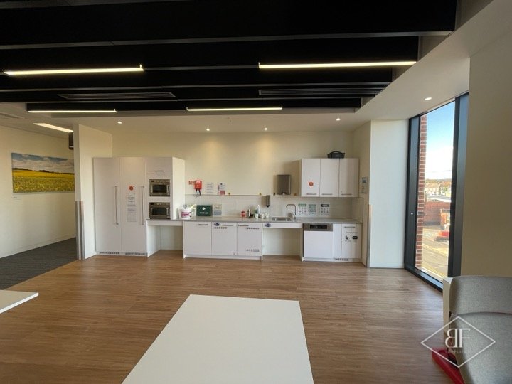 Bright welfare kitchen with white units and microwaves along a wall of tall windows