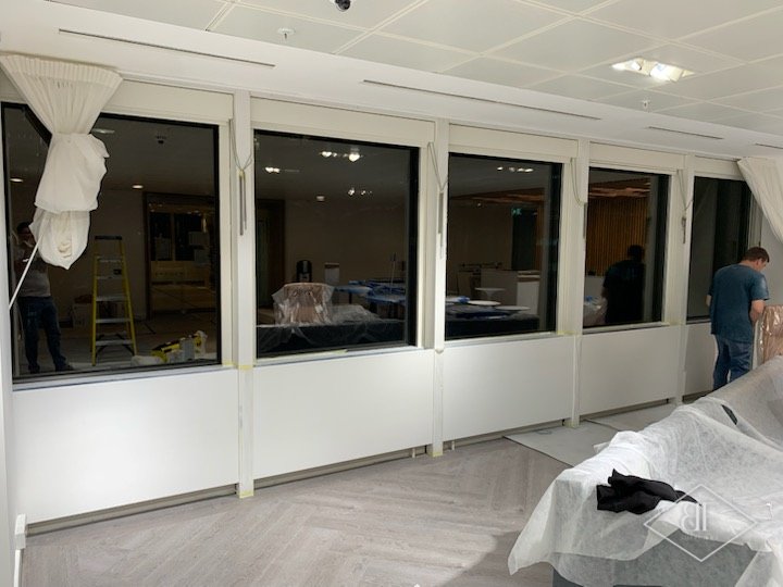 Row of office windows with freshly sprayed white panels below and dust sheets