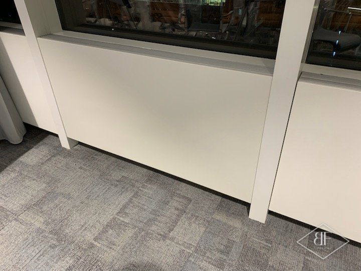 Close view of smooth white sprayed panels and mullion above office carpet tiles