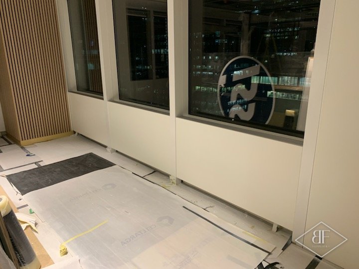 Resprayed white office wall panels beside a slatted timber feature, with floor protection in place
