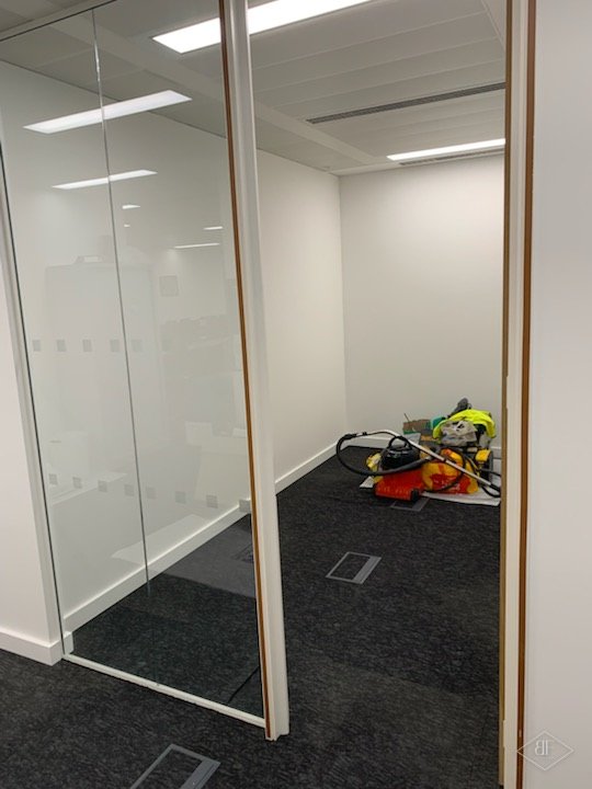 Glass partition and door frame leading into a small room with cleaning equipment