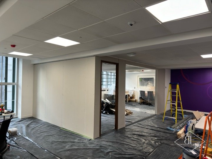 Boarded partition with doorway opening during works, dust sheets covering the carpet