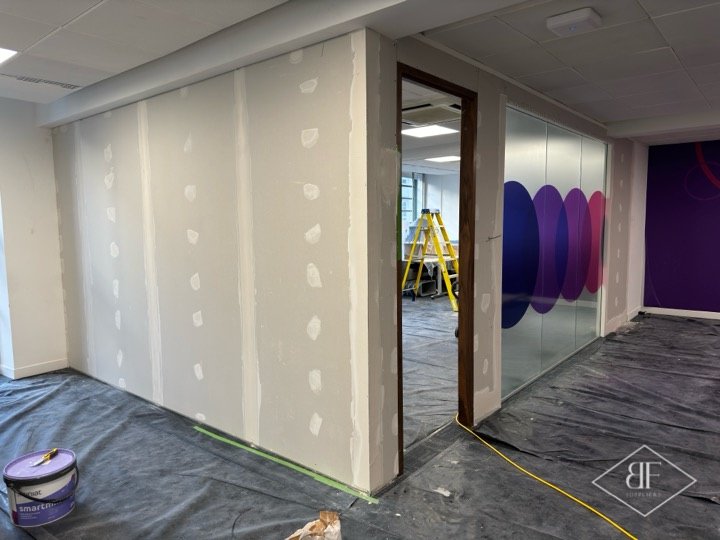 Plasterboard partition awaiting finishing, with glazed section and ladder beyond