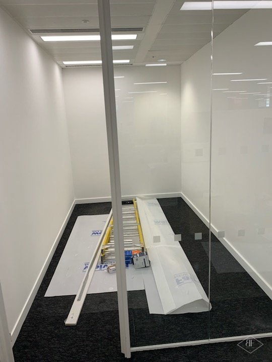 Glazed meeting room partition with timber frame and white walls, carpet being protected