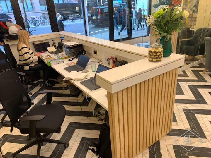 L-shaped reception desk with vertical oak slats and staff working behind it in a London office