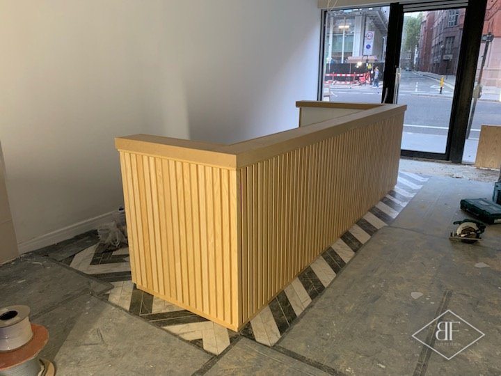 Newly fitted slatted reception desk on a part-finished floor beside a large glazed frontage
