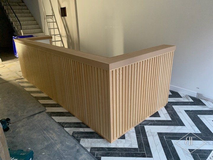 Corner of the slatted reception desk on the chevron floor, with a staircase behind