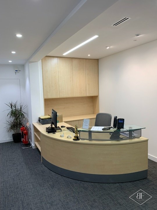 Curved light timber reception desk with glass top in an office with grey carpet