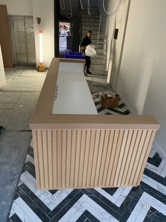 Narrow slatted reception desk installed in hallway with chevron tiled floor