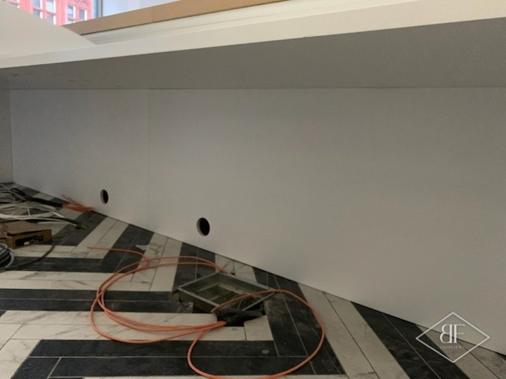 Rear of reception desk showing white panelling and cable routing holes