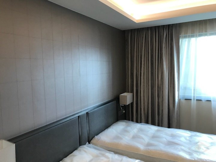 Bedroom with panelled wall, wooden bed headboard and curtains beside the window
