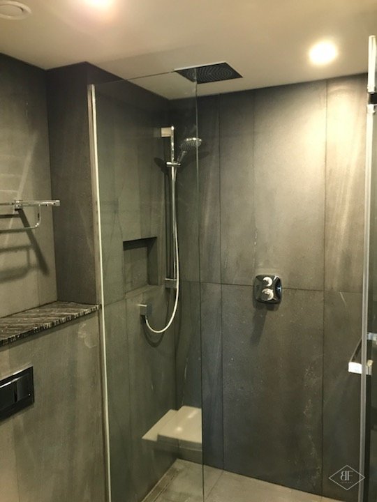 Walk-in shower with large dark tiles, glass screen and built-in seat