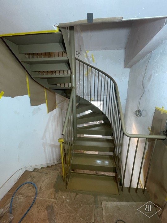 Spiral staircase base coat sprayed olive green with surrounding surfaces protected