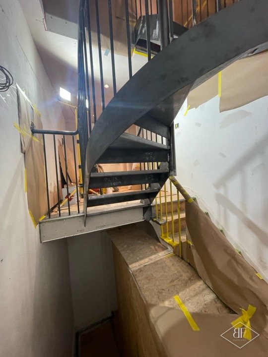 Upper flight of a spiral steel staircase with dark finish and masking