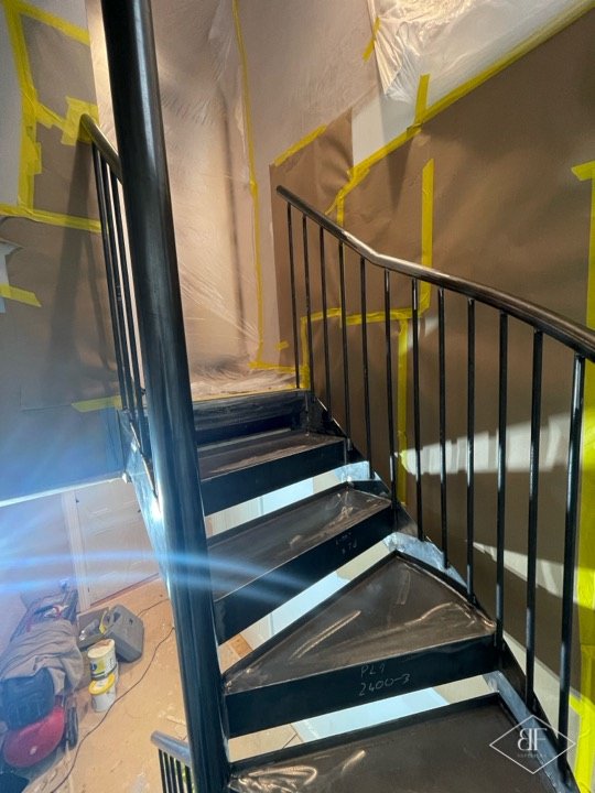 Dark sprayed steel treads and balusters with yellow masking tape on the walls