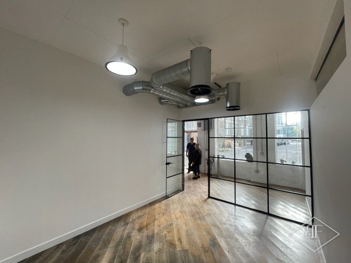 Narrow room with exposed ducting leading to steel-framed glazed partition