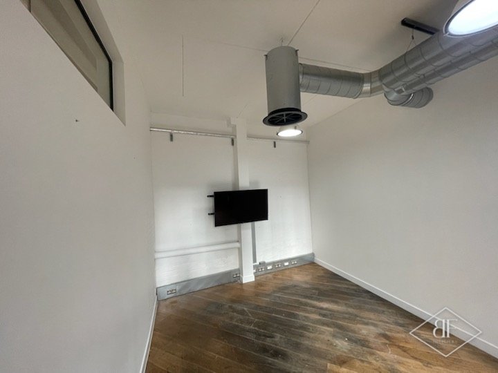 Empty white room with wall-mounted screen, exposed ductwork and worn timber floor