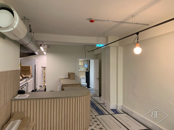Curved slatted service counter during fit-out, with ducting overhead and floor protection down