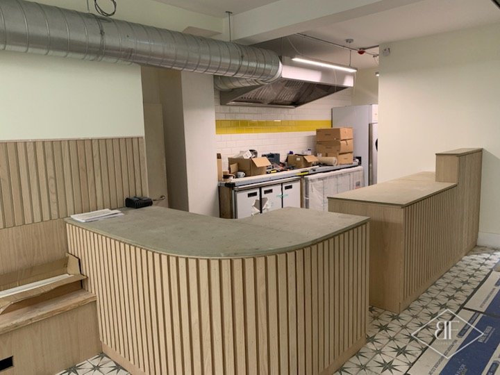 Oak slatted curved counter and tall counter end before opening, with the kitchen beyond