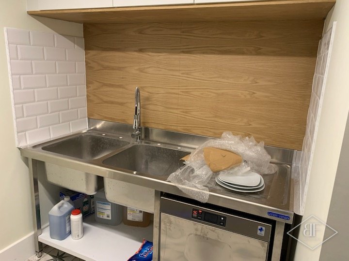 Stainless steel sink and dishwasher beneath an oak panelled splashback and white tiles