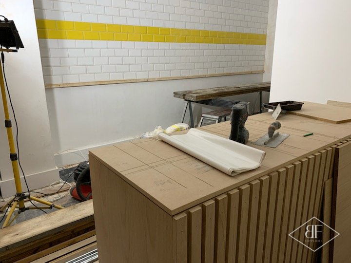 Slat cladding being fitted to bar unit against white tiled wall with yellow stripe