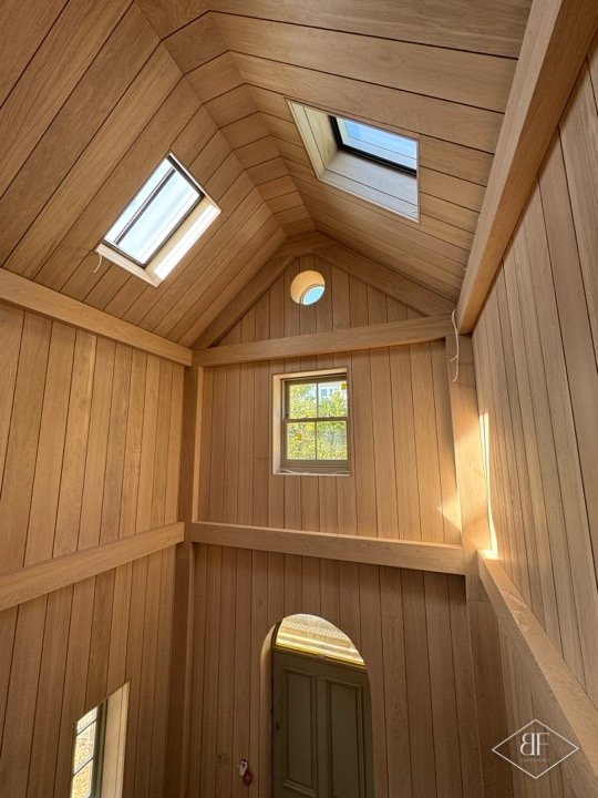 Tall oak panelled gable room with two rooflights, a small window and an arched door