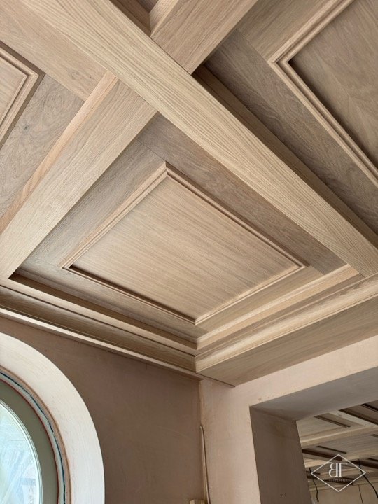 Close view of layered oak coffer beams meeting at a corner above an arched window