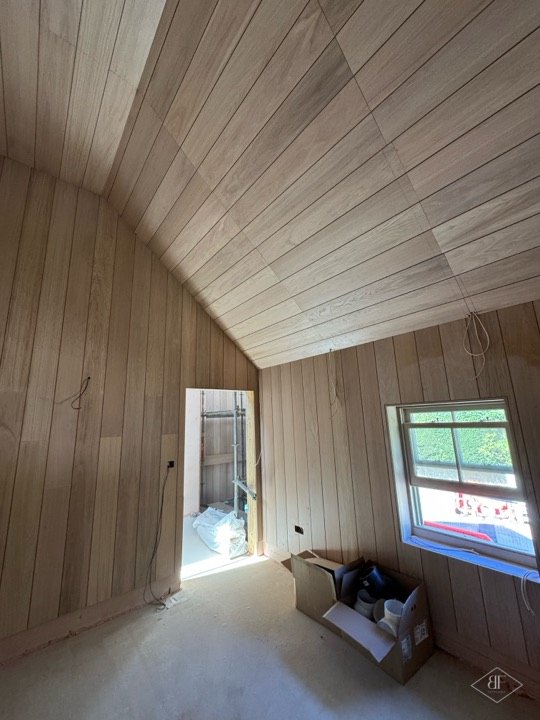 Oak boarded sloping ceiling and wall panelling in a bedroom with a small window