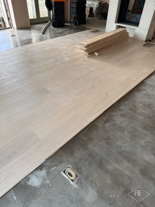 Oak flooring boards laid out over a screeded floor, with a stack of boards waiting