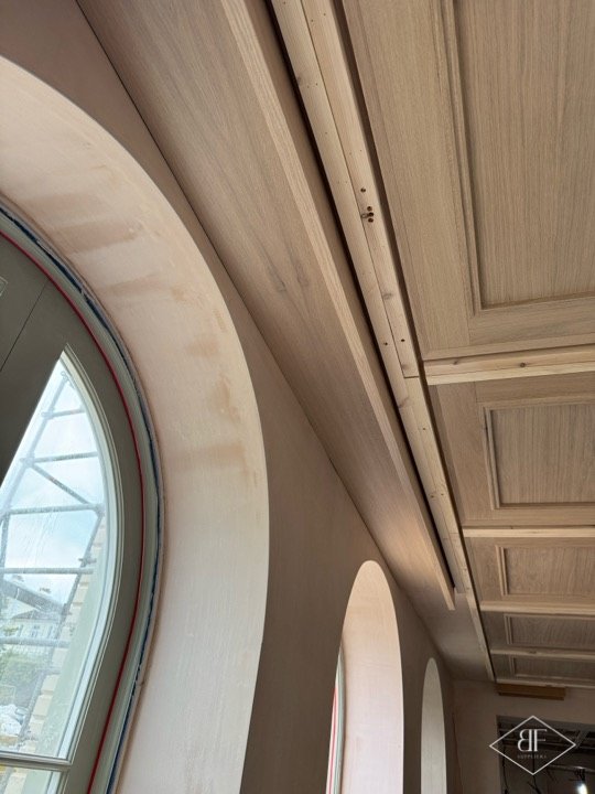 Arched window lining beside coffered oak ceiling panels, finished carpentry