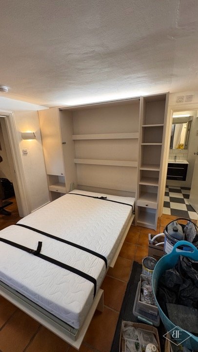 Wall bed in the lowered position in a basement flat with a bathroom visible beyond