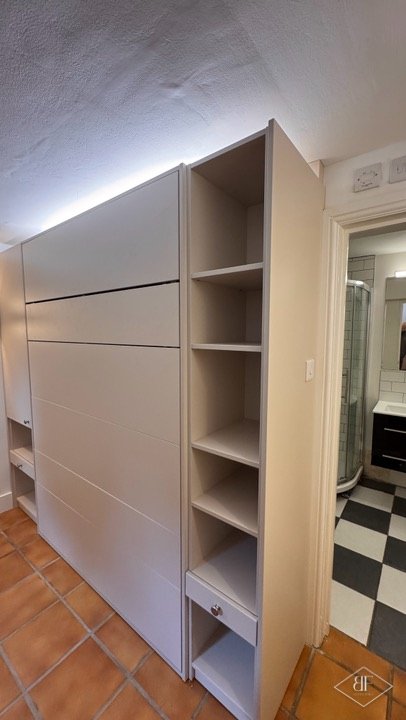 Tall open shelving beside the closed wall bed unit with a bathroom doorway behind